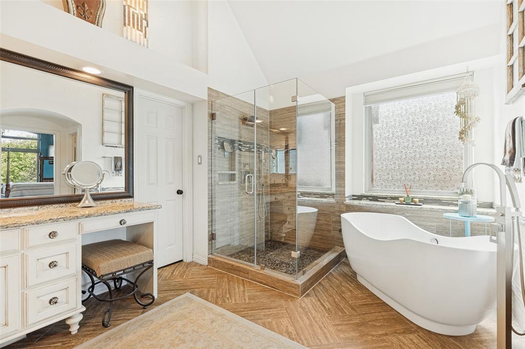 Bathroom featuring a freestanding soaking tub, walk-in glass-enclosed shower with tiled surround, stone-top vanity with built-in cabinetry, and wood-finish herringbone flooring