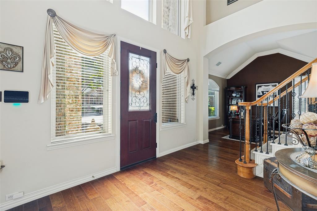 Two-story foyer with high ceilings, wood-finish flooring, an arched entryway, and a solid wood front door featuring decorative glass inlay, complemented by a staircase with iron balusters and a wood handrail