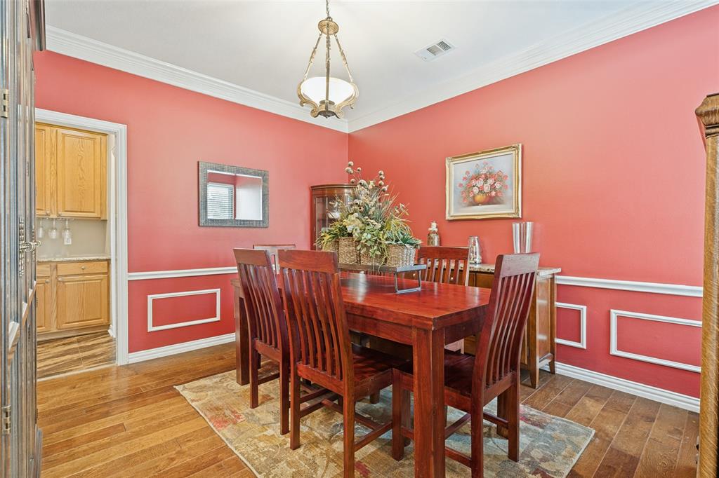 Dining area featuring crown molding, custom wall wainscoting, wood-finish flooring, and a decorative pendant light fixture