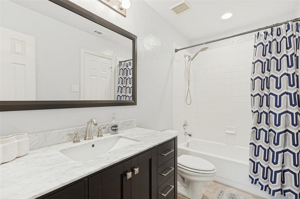 Dark wood vanity cabinet featuring a stone-top counter, undermount sink with a metallic finish faucet, large framed mirror, and a tub-shower combination with tiled surround