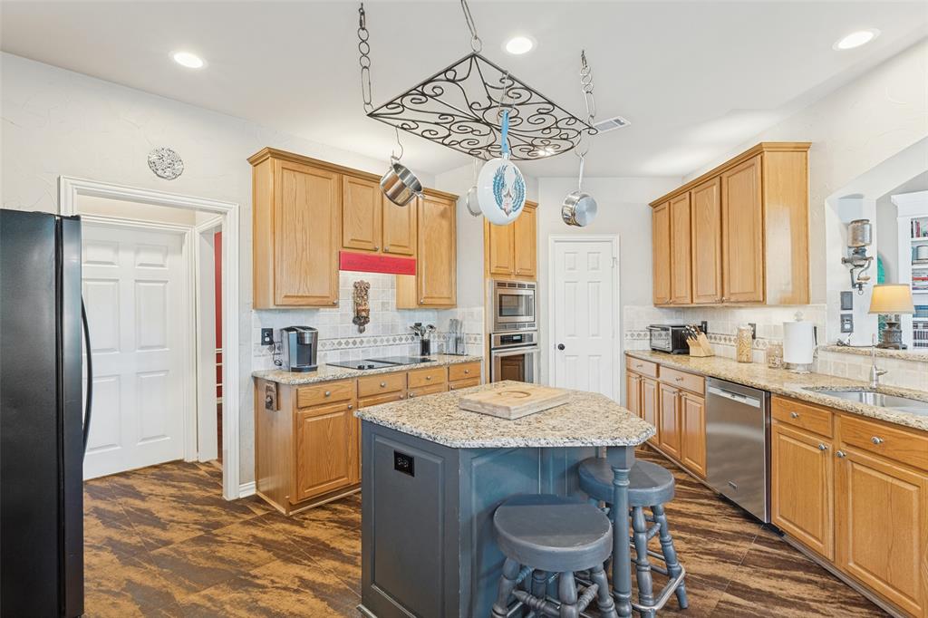 Kitchen featuring cabinetry with a natural finish, stone countertops, central island, stainless steel built-in oven, and wood-finish flooring