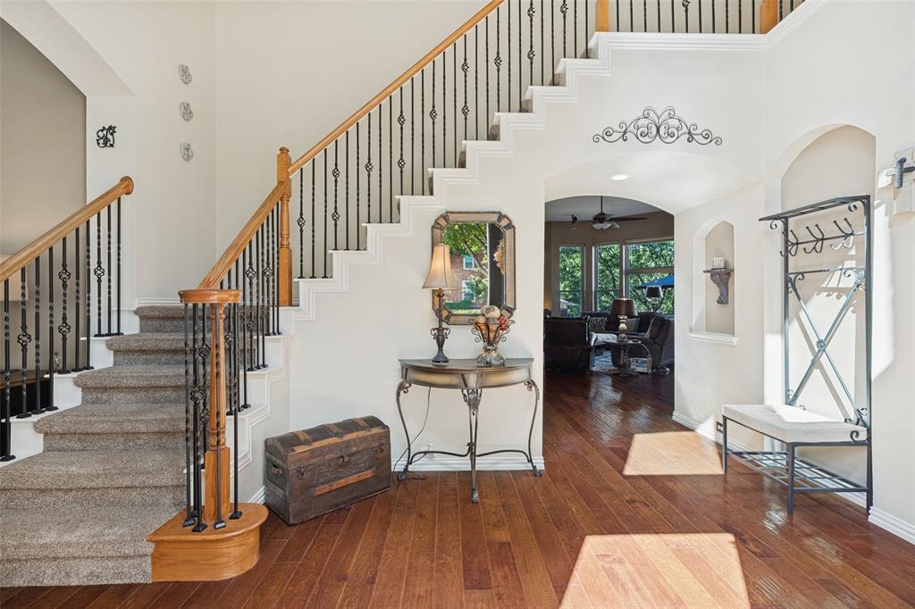 Grand foyer featuring wood-finish flooring, a staircase with a wooden handrail, decorative iron balusters, and a recessed arched wall niche