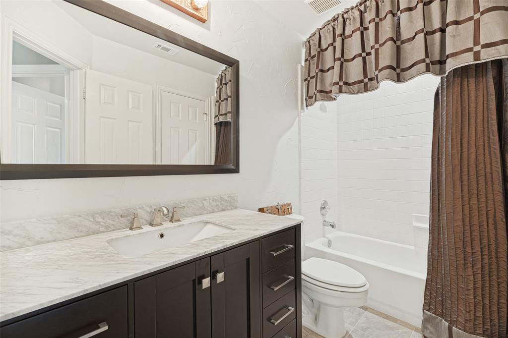 Bathroom featuring a dark-finish vanity cabinet, stone-surface countertop with an integrated basin, large framed mirror, and a tile-surround shower and tub combination