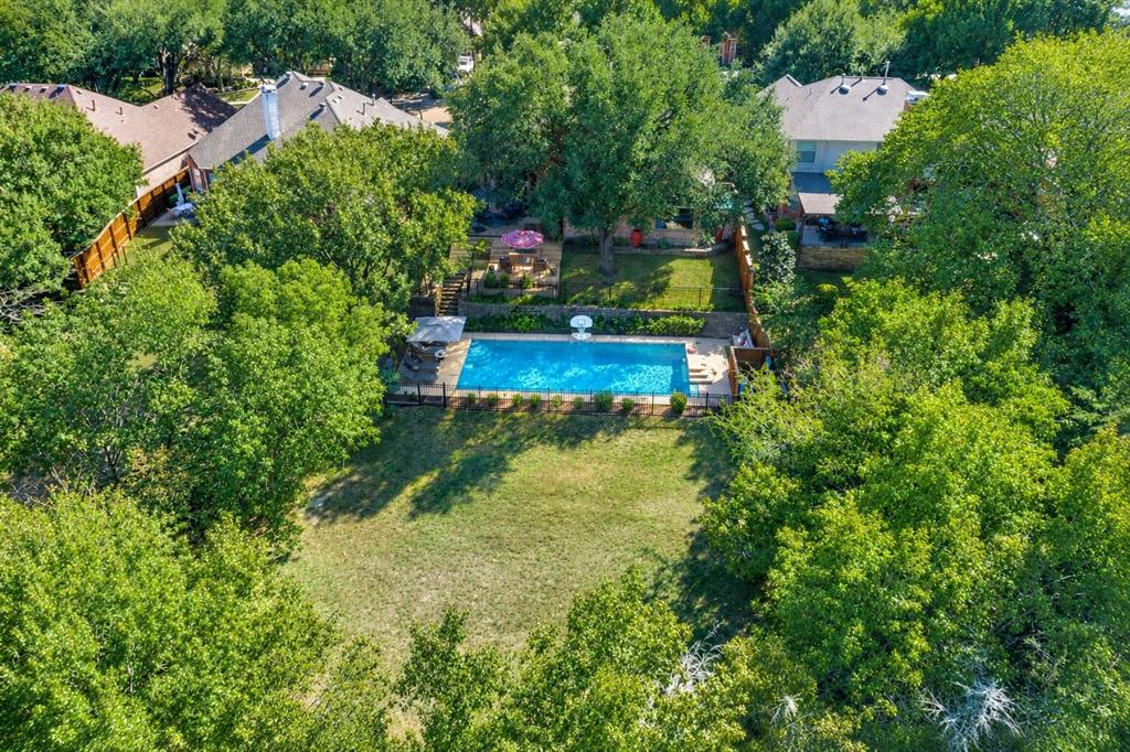 Expansive backyard featuring an in-ground swimming pool, stone retaining wall, paved patio area, and mature trees