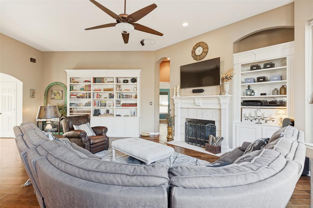 Living area featuring wood-finish flooring, a fireplace with a white mantel, built-in shelving, arched doorways, and a ceiling fan