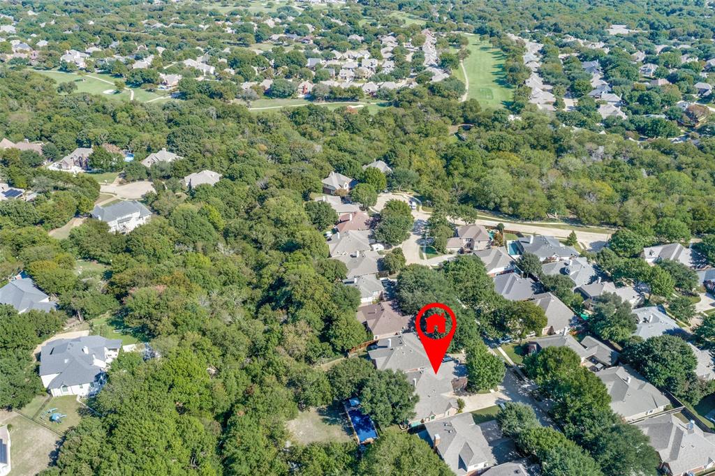 Aerial perspective of a residential property featuring a backyard swimming pool, stone-surface roofing, and dense perimeter tree canopy