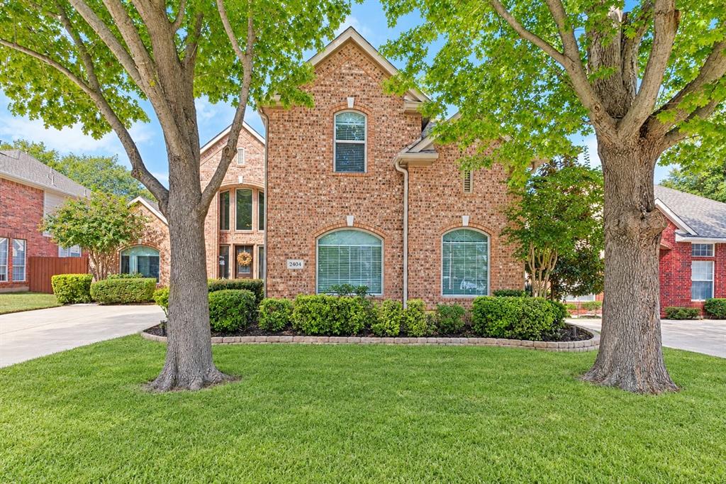 Brick exterior featuring an arched entryway, stone-edged garden beds, multi-pane windows with arched detailing, and a concrete driveway