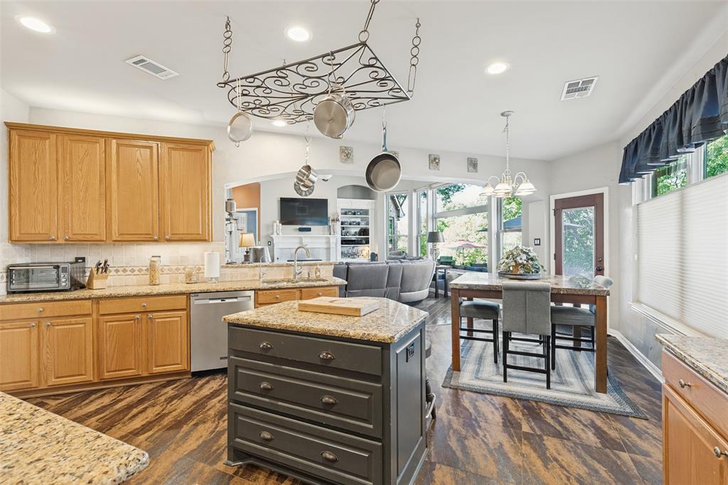 Kitchen featuring natural-finish wood cabinetry, stone countertops, a central island with storage drawers, decorative metal pot rack, and wood-finish flooring