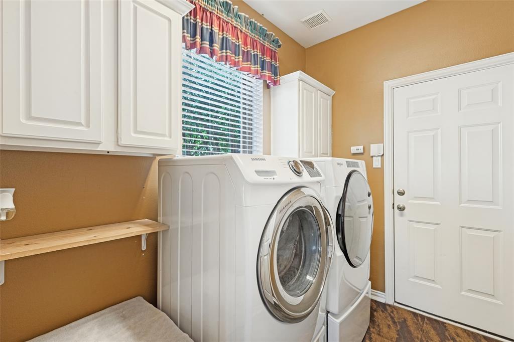Laundry room featuring white shaker-style wall cabinets, a natural wood floating shelf, and wood-finish flooring