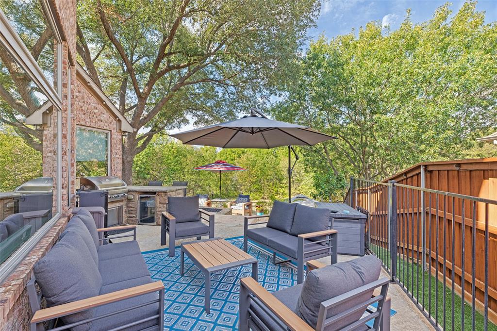 Outdoor patio featuring a built-in stone grill station, concrete paver flooring, a vertical iron fence, and a brick exterior wall