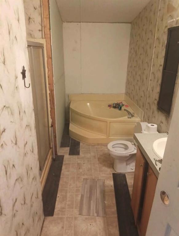 Corner soaking tub with integrated surround, enclosed shower stall, vanity with integrated sink, and dual-finish flooring