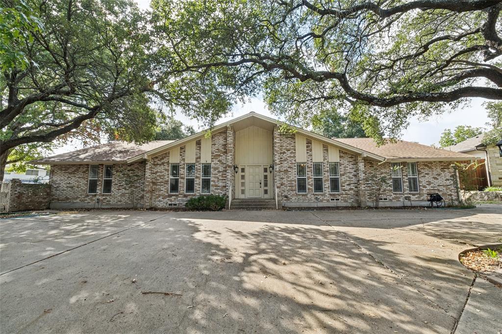 Brick exterior featuring a multi-gabled roofline, expansive paved driveway, and mature oak tree canopy