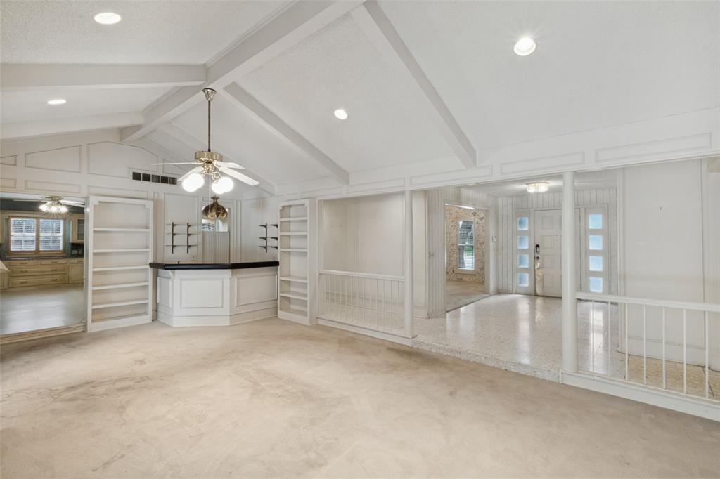 Vaulted ceiling with exposed beams, built-in cabinetry, custom wet bar, recessed lighting, and tiered levels with balustrade railings