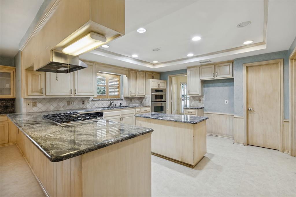 Kitchen featuring light wood-finish cabinetry, kitchen island, granite countertops, convection oven and microwave, a gas cooktop and recessed ceiling lighting