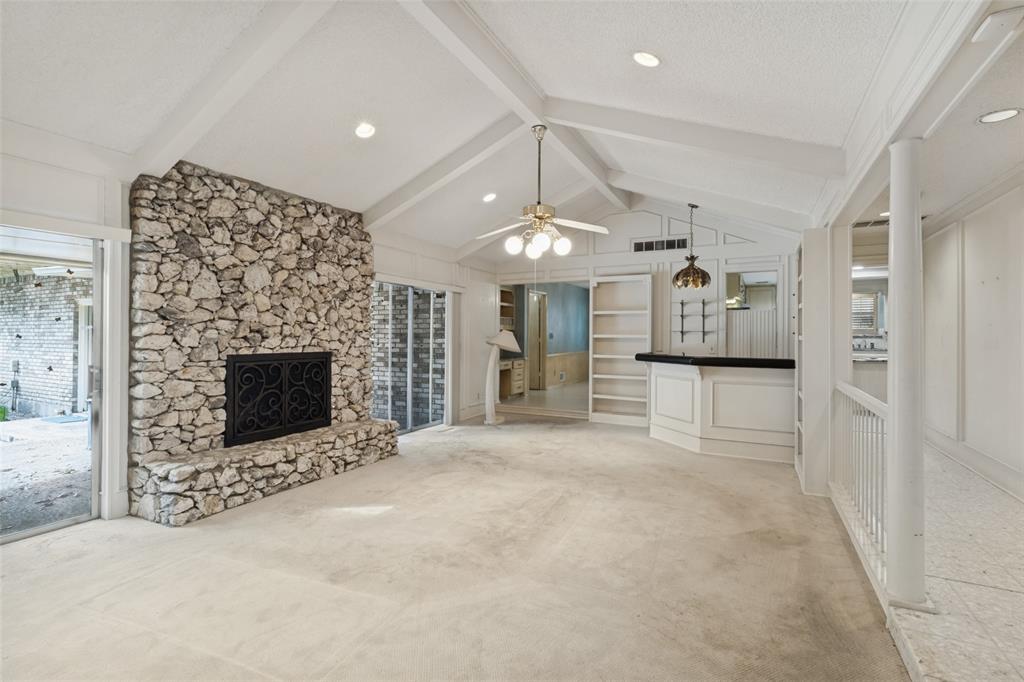 Vaulted ceilings with exposed beams, floor-to-ceiling stone fireplace, built-in wet bar, and recessed lighting