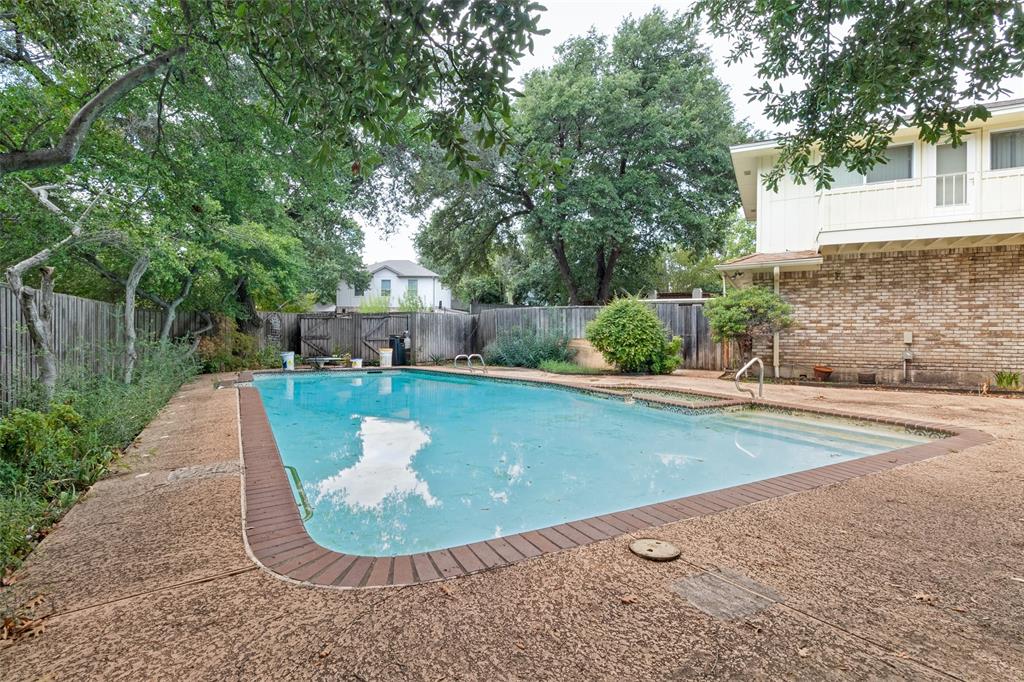 In-ground swimming pool with a brick-trimmed edge, aggregate concrete decking, and mature landscaping enclosed by a wood privacy fence