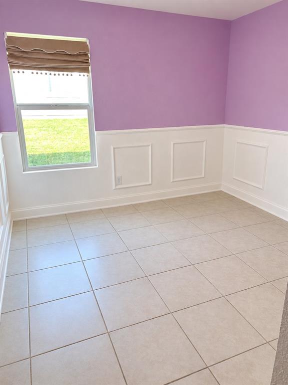 Interior space featuring large-format tile flooring, crisp white wainscoting with classic picture-frame molding, and a single-hung window