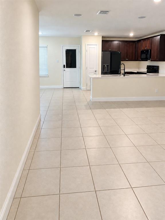 Kitchen featuring dark wood cabinetry, a light-toned solid surface countertop with an integrated basin, a faucet with a high-arch spout, and large-format tile flooring