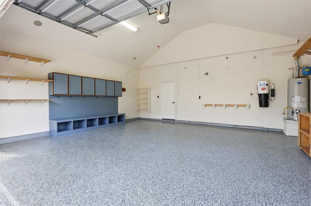 Attached garage featuring an epoxy-coated floor, vaulted ceiling, built-in cabinetry with beadboard detailing, additional wall-mounted shelving, and an integrated central vacuum system