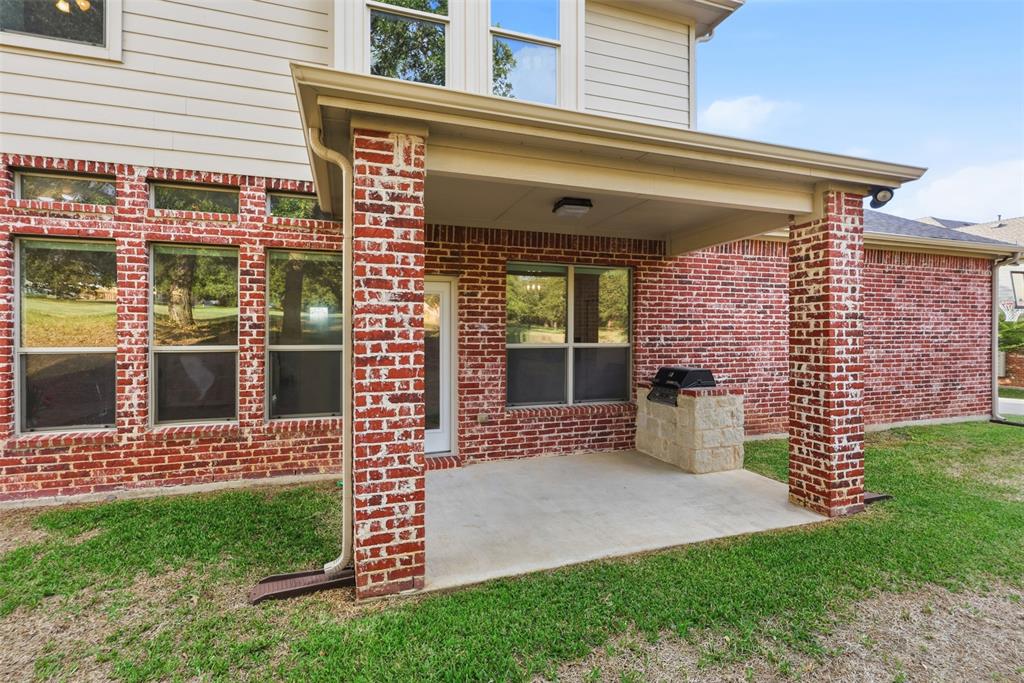 Covered rear patio featuring brick columns, concrete flooring, and a built-in stone grill station