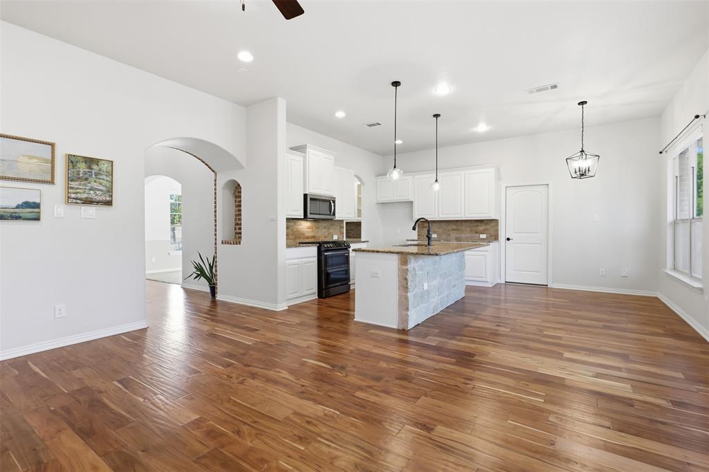 Kitchen featuring white cabinetry, wood-finish flooring, a stone-accented center island with countertop seating, recessed lighting, and a brick-lined arched architectural niche