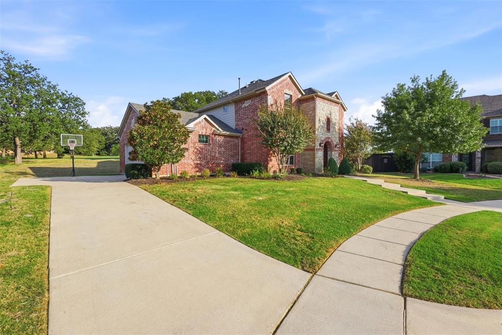 Two-story exterior featuring multi-toned brick and stone masonry, concrete driveway, and established landscaping