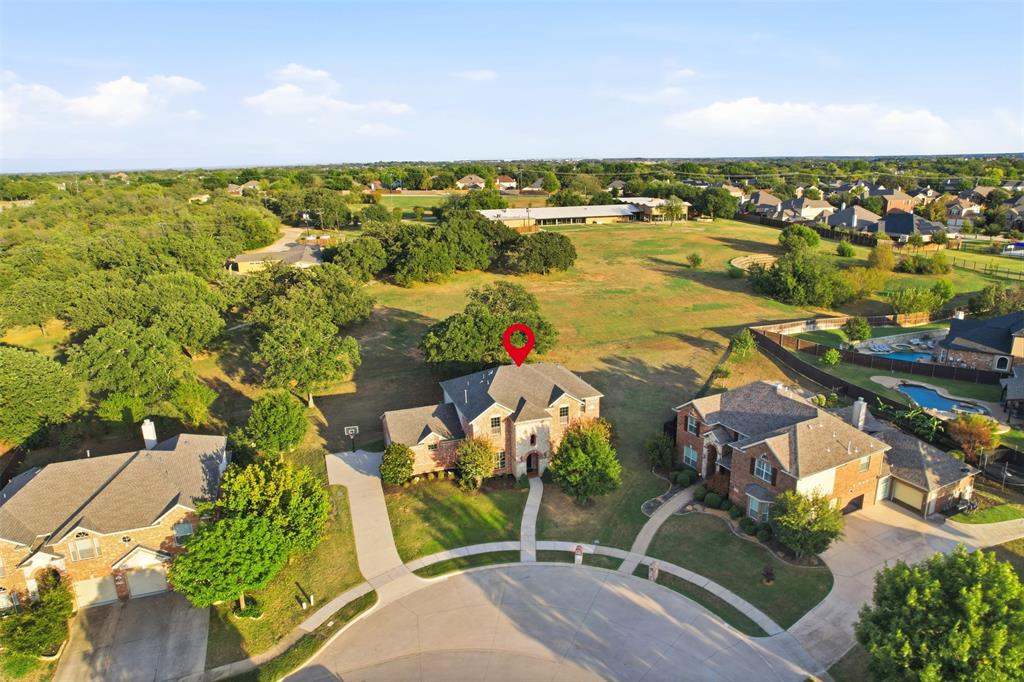 Aerial view of residential property featuring a multi-story brick exterior, attached multi-car garage, concrete driveway, and expansive acreage