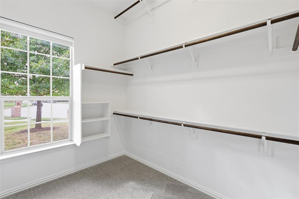 Storage space featuring tiered shelving, integrated clothing rods, and a multi-level built-in organizer, finished with neutral wall-to-wall carpeting and a window with natural lighting