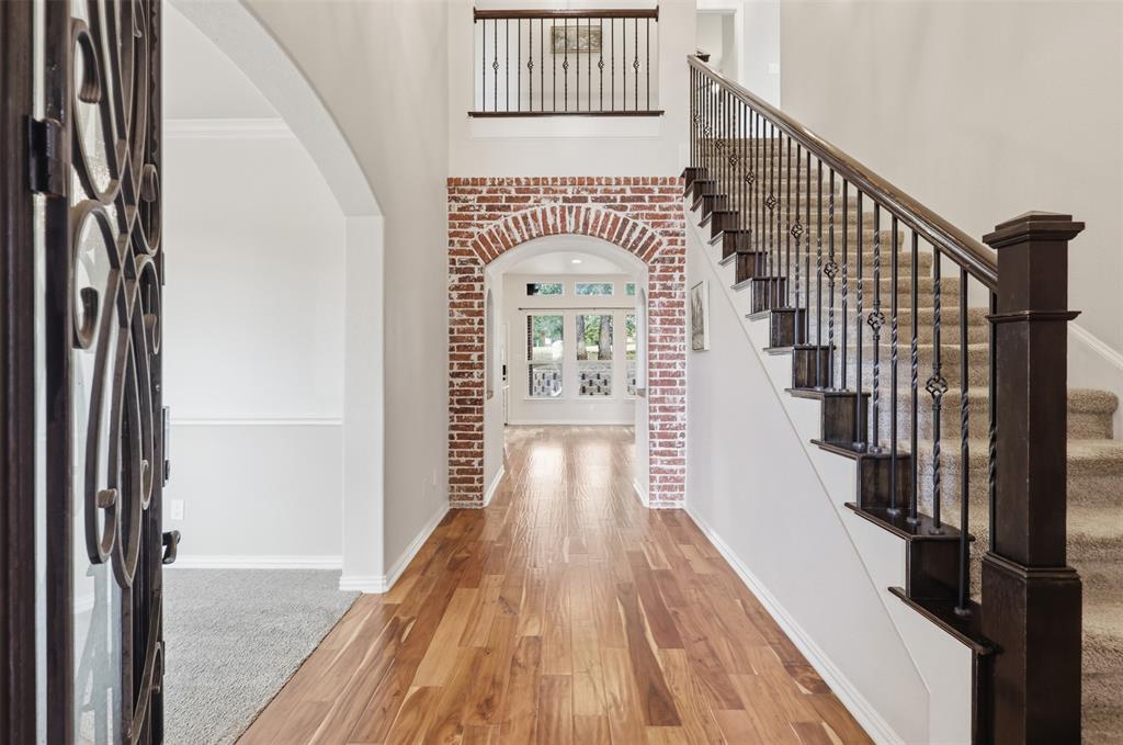 Foyer featuring wood-finish flooring, a decorative arched brick entryway, staircase with metal balusters and dark-stained handrail, and high ceilings