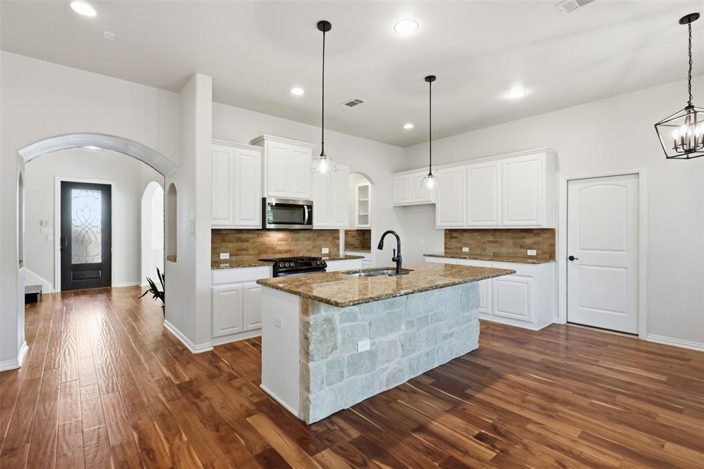Kitchen featuring white cabinetry, stone-clad island base, wood-finish flooring, stone-tiled backsplash, and geometric pendant lighting