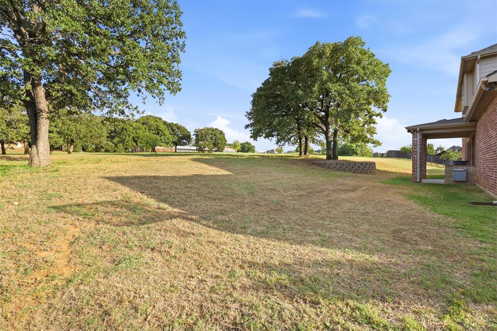 Expansive grounds featuring mature shade trees, a segmented retaining wall, and a covered brick patio