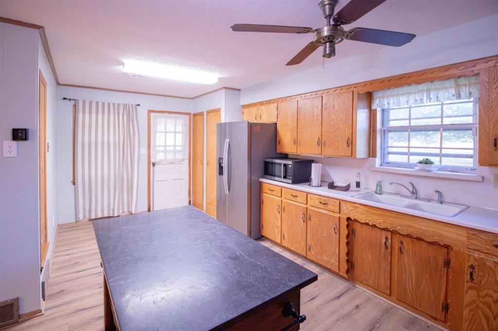 Kitchen featuring wood cabinetry, integrated central island with dark surface, stainless steel refrigerator, white dual-basin sink, and wood-finish flooring