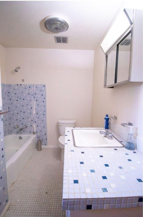 Bathroom featuring a mosaic-tiled countertop with an integrated sink, a shower-tub combination with matching mosaic tile surround, and a wall-mounted mirrored medicine cabinet