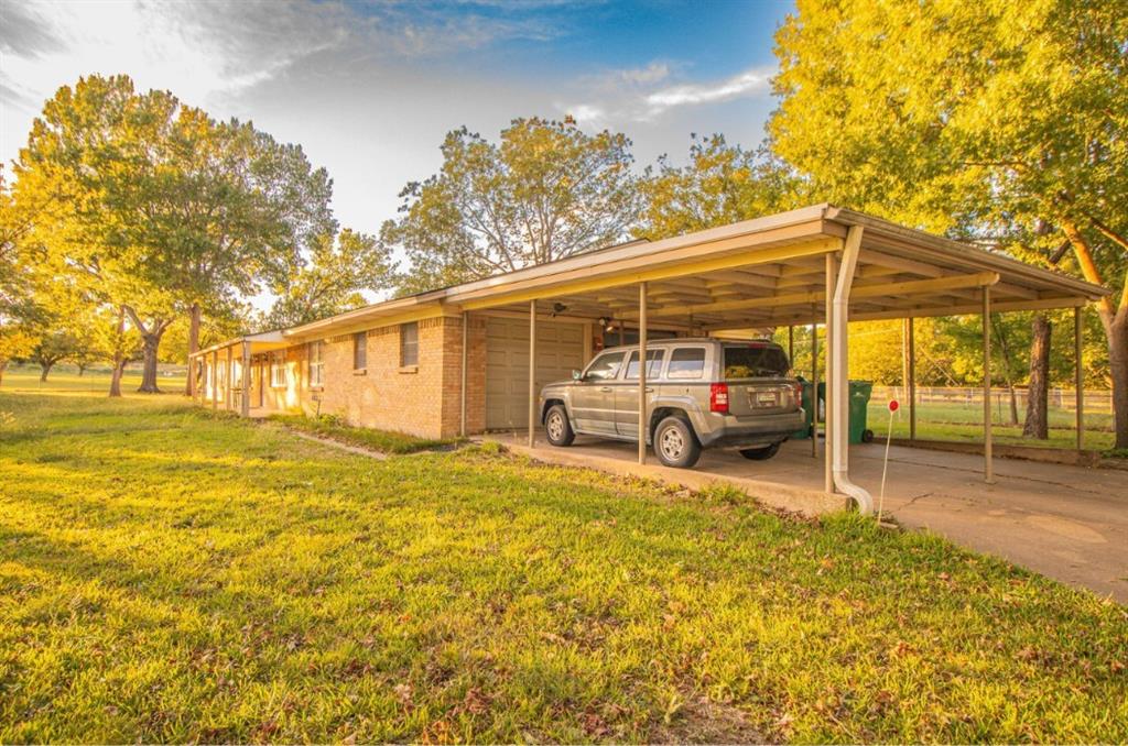 Single-story brick exterior featuring an attached carport, concrete driveway, and expansive lawn with mature trees