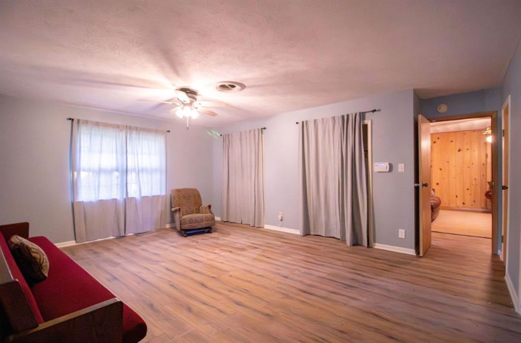 Spacious room featuring wood-finish flooring, a ceiling-mounted light fixture with fan, and multiple closets