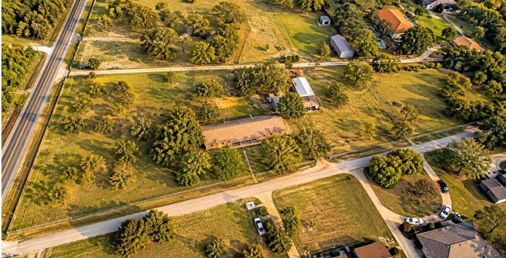 Aerial perspective of a sprawling lot featuring mature shade trees, expansive grass fields, a detached metal-roof outbuilding, and direct frontage to paved roads