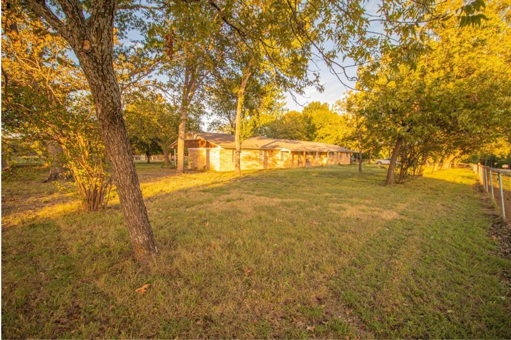 Expansive grounds featuring mature shade trees, a brick exterior, and perimeter fencing