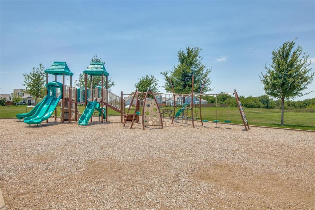 Outdoor recreation area featuring a multi-level structure with dual slides, a climbing wall, a swing set, and a gravel base