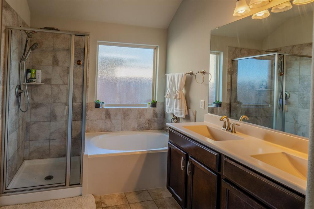 Bathroom featuring a dual-sink vanity with dark-finish cabinetry, a separate soaking tub, a tiled walk-in shower with glass enclosure, and a full-width vanity mirror