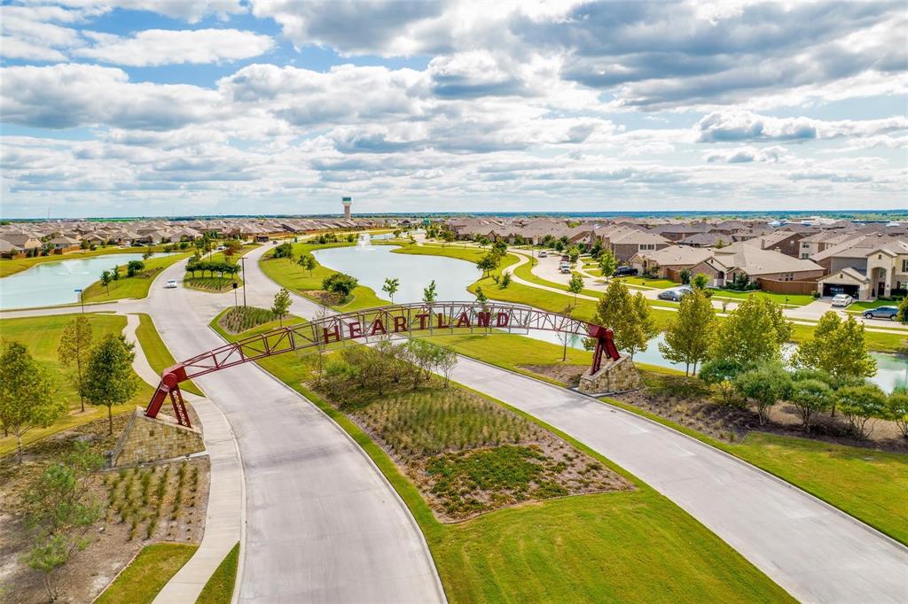 Community entrance featuring a metal arch structure, stone-based supports, ornamental ponds, manicured landscaping, and concrete walkways