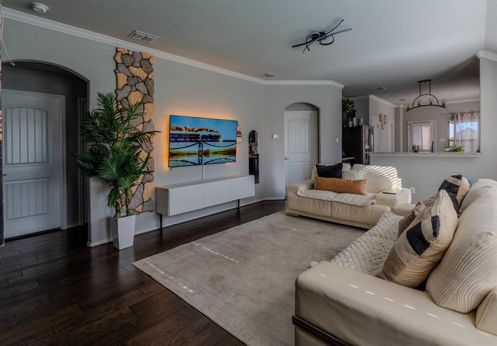 Dark wood-finish flooring, accent wall featuring natural stone masonry, arched doorways, crown molding, and a pass-through opening to the kitchen area