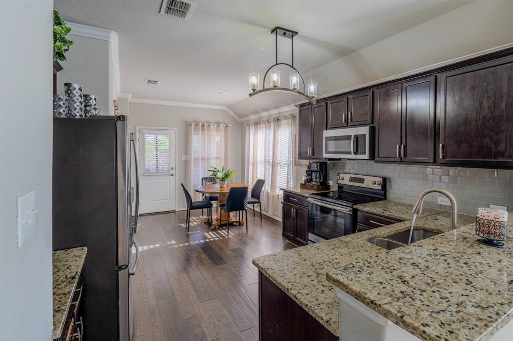 Kitchen featuring dark wood cabinetry, stone countertops, subway tile backsplash, stainless steel appliances, and wood-finish flooring