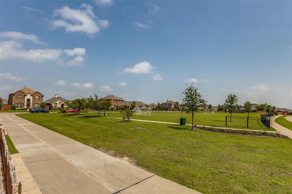 Expansive green space featuring a concrete pathway, mature trees, and metal perimeter fencing