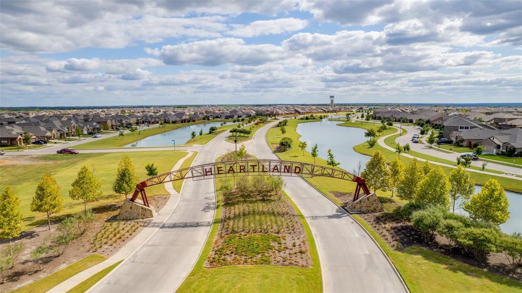 Community entrance featuring a metal architectural archway, stone pillar foundations, paved roadways, retention ponds, and landscaped green space
