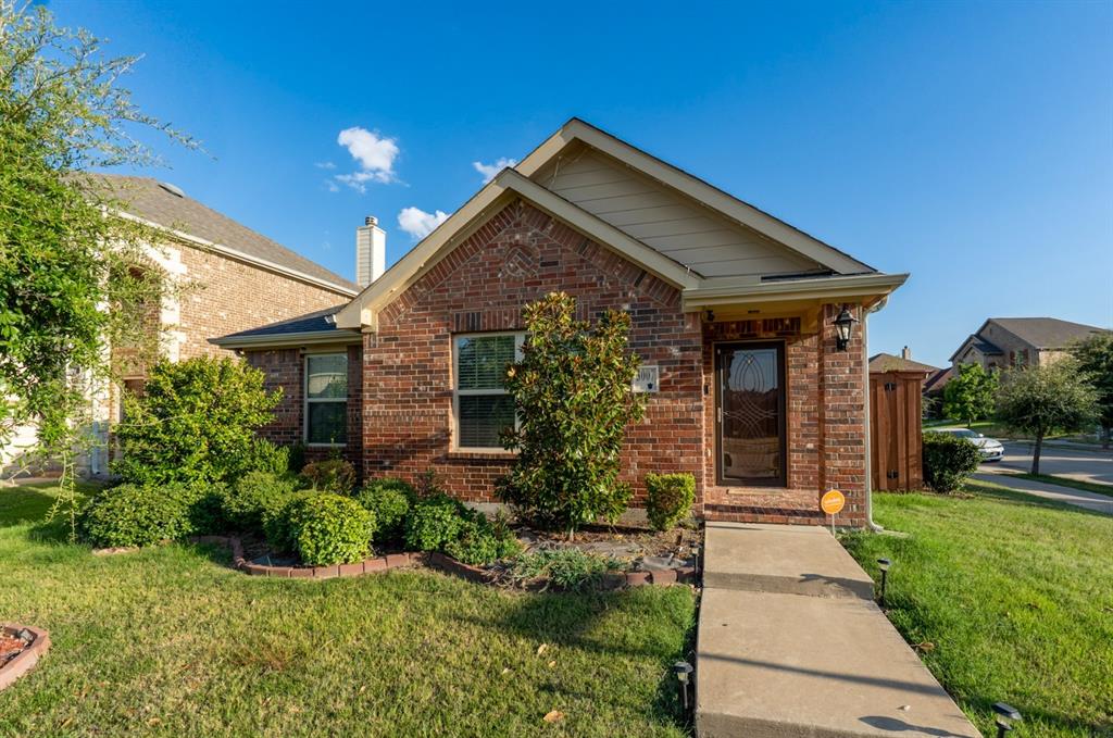 Single-story residence featuring a brick exterior, gable roofline, covered entryway with a decorative glass-panel front door, and manicured landscaping