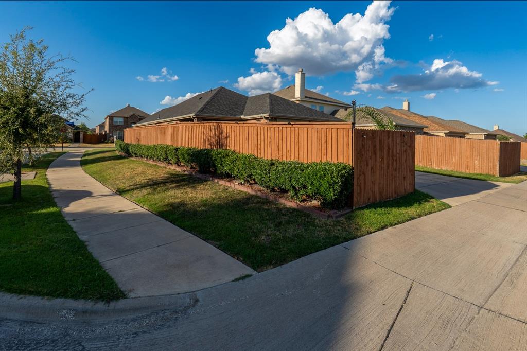 Corner lot exterior featuring a wood privacy fence, concrete sidewalk, manicured hedging, and grass lawn