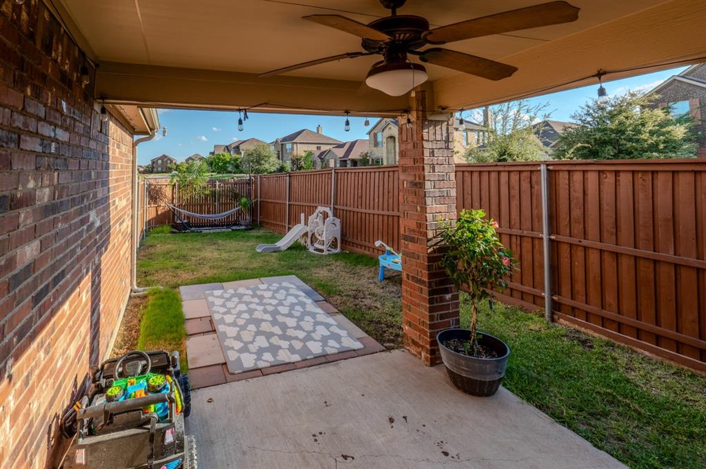 Covered patio featuring a brick-column support, ceiling fan, and concrete flooring, complemented by a fenced backyard with a stone-paver accent area