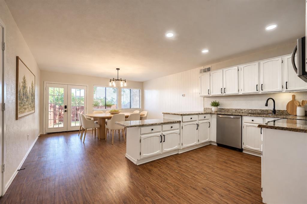 Kitchen featuring white cabinetry, stone-finish countertops, stainless steel dishwasher, wood-finish flooring, and double glass-paneled exterior doors Kitchen featuring white cabinetry, stone-finish countertops, stainless steel dishwasher, wood-finish flooring, and double glass-paneled exterior doors