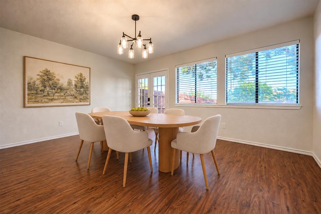 Wood-finish flooring, six-light metal chandelier, and large dual-pane windows with horizontal blinds, complemented by glass-paneled exterior door