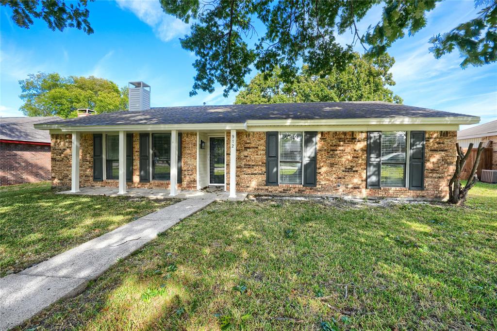 Single-story brick exterior featuring a covered front porch, dark-tone shutters, shingled roof, and a concrete walkway